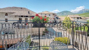 A balcony with metal railings, a table, and chairs, overlooking a residential area with houses and mountains in the background. - Apartment 'Odorizzi Dolomiti Di Brenta' with Mountain View, Shared Garden and Balcony (Tassullo)