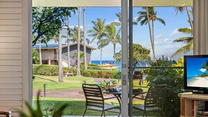 A room with a sliding glass door leading to a balcony with a view of the ocean and palm trees. - Unwind in Napili, as sunsets await (Napili)