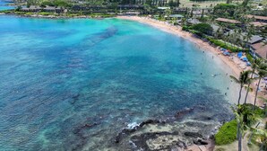 A coastal resort with a sandy beach, clear turquoise waters, and a backdrop of lush greenery and buildings. - Unwind in Napili, as sunsets await (Napili)