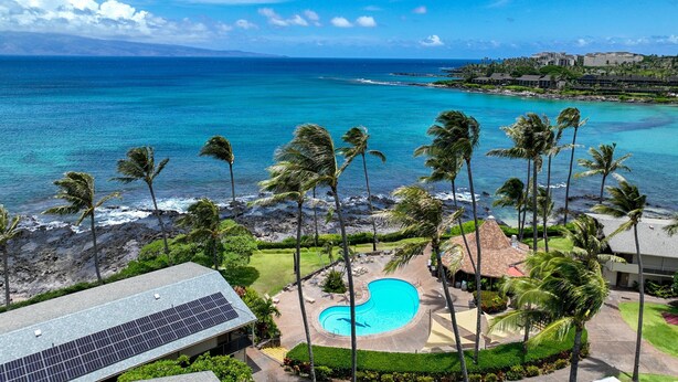 A resort with a swimming pool surrounded by palm trees, a view of the ocean, and a building with solar panels. - Unwind in Napili, as sunsets await (Napili)