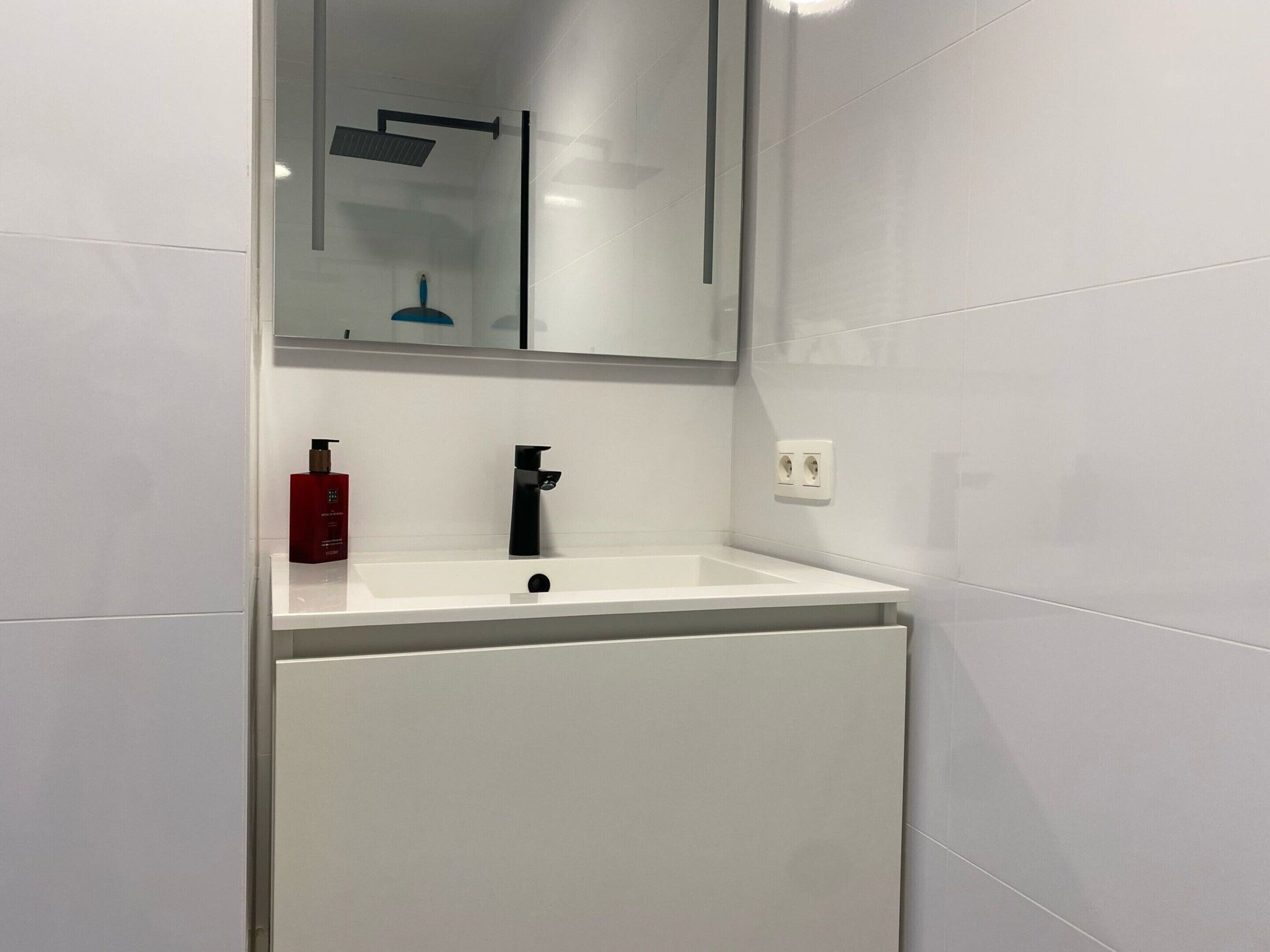 Ein modernes Badezimmer mit einem weißen Waschbecken, einem schwarzen Wasserhahn und einem Spiegel darüber.