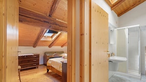 A bedroom with a wooden ceiling, a bed, a dresser, and a bathroom with a sink and shower. - Apartment 'Odorizzi Lago Di Tovel' with Mountain View and Shared Garden (Tassullo)