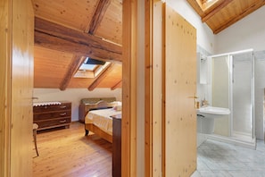 Une chambre avec un plafond en bois, un lit, une commode et une salle de bain équipée d’un lavabo et d’une douche.