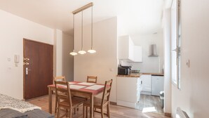 A dining area with a wooden table and chairs, a kitchen in the background, and a door to the left.