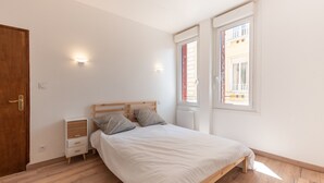 A bedroom with a wooden bed, two bedside tables, a wardrobe, and a window with blinds.