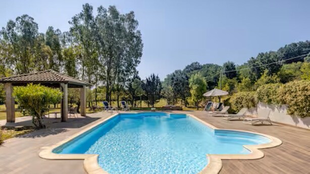 En rektangulär swimmingpool med ett kaklat poolområde, omgiven av solstolar och en pergola.