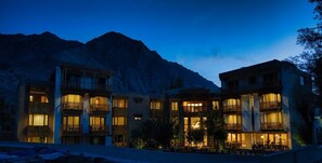 A multi-story hotel with balconies and warm lighting, set against a mountainous backdrop. - Hotel Stendel (Diskit)