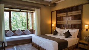 A bedroom with a large bed, a window seat with cushions, a wooden headboard, and bedside lamps. - Hotel Stendel (Diskit)