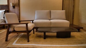 A living room with a sofa, armchair, and coffee table, featuring a wooden floor and a textured rug. - Hotel Stendel (Diskit)
