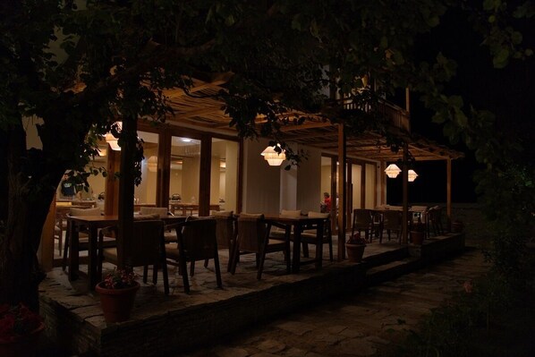 An outdoor dining area with tables and chairs, surrounded by trees and a wooden pergola. - Hotel Stendel (Diskit)