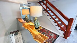 A wooden console table with a lamp and a decorative item, a red patterned rug, and a wooden staircase. - Historical Mattocks House - Waterfront, Downtown Swansboro, Boat Slip (Swansboro)