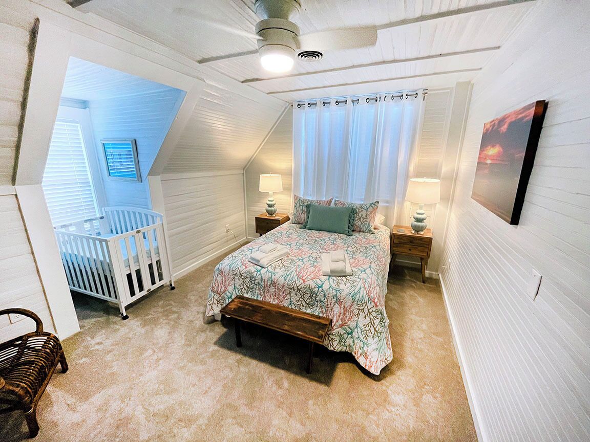 A bedroom with a bed, a crib, a bench, and a nightstand with lamps.