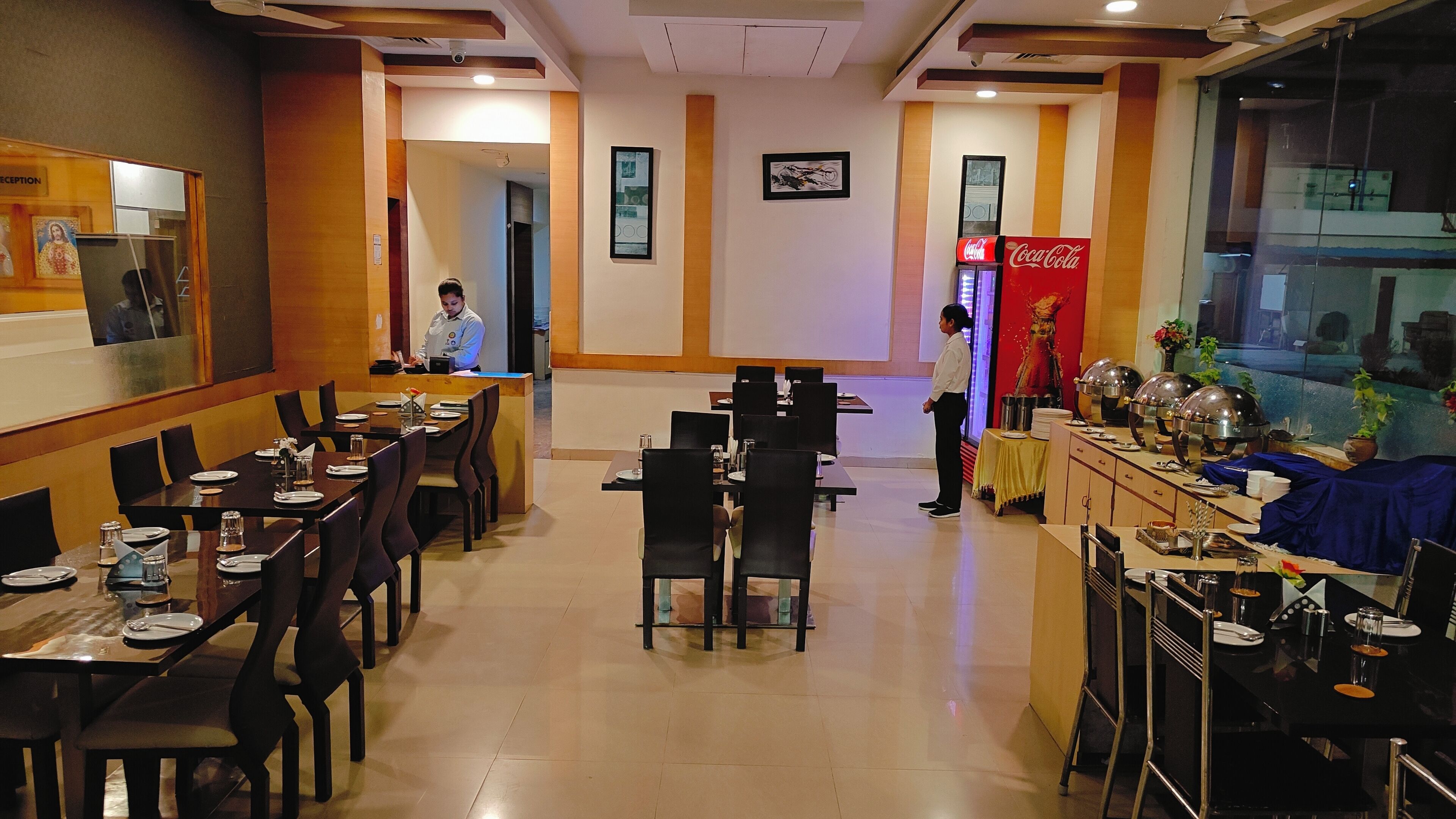 A restaurant with multiple dining tables and chairs, a reception area, and a Coca-Cola sign.