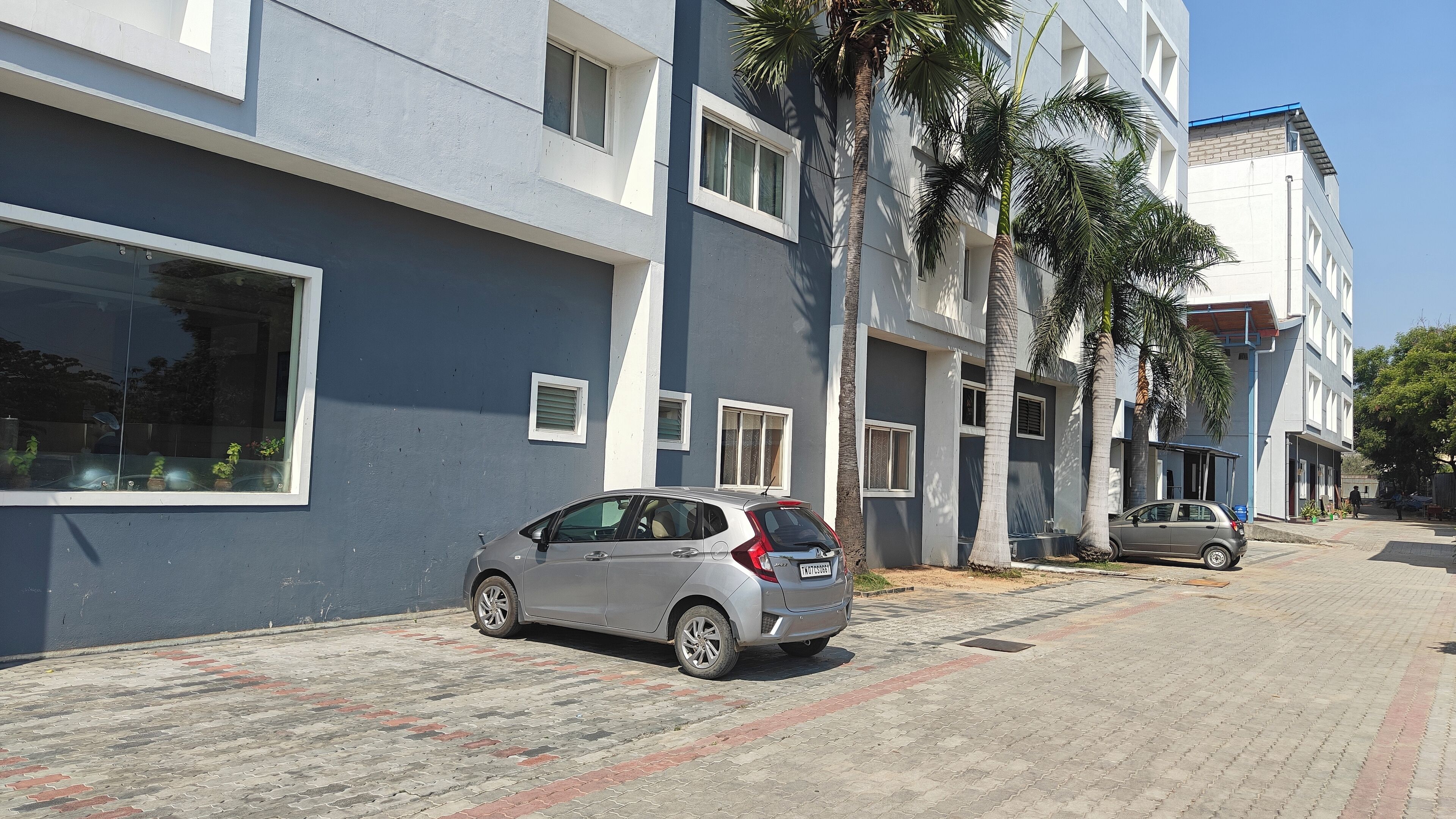 A modern building with a grey facade, multiple windows, and a paved driveway.