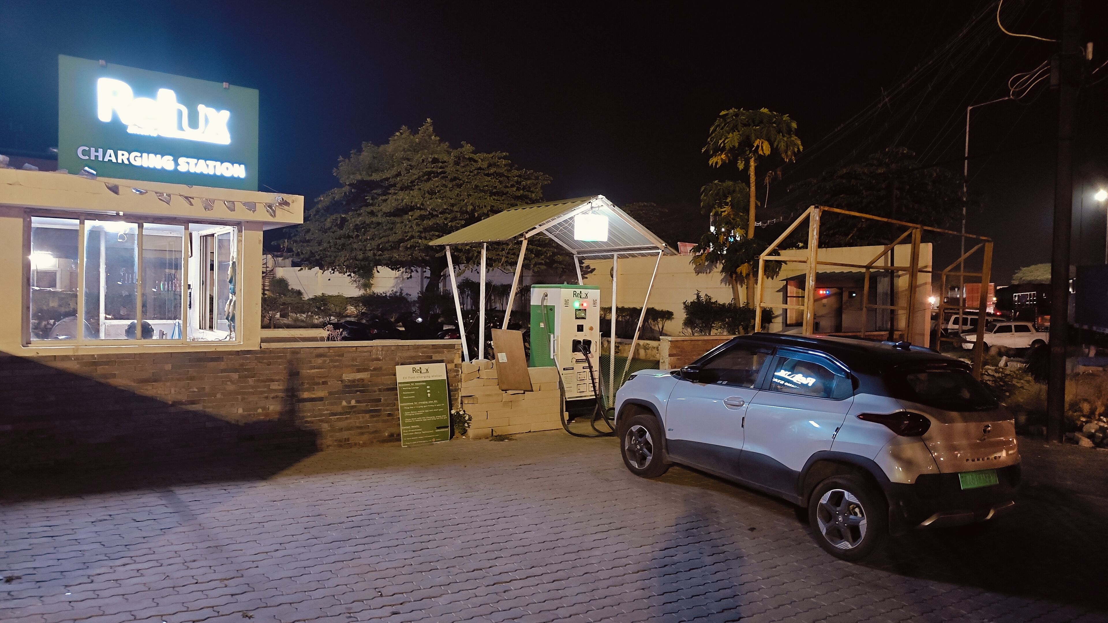 Una stazione di ricarica con un cartello, un'auto parcheggiata e un edificio con insegna.