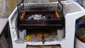 A portable grill with a metal grate, placed on a white stand with a stone wall in the background. - 9, Cimo da aldeia (Aldeia de João Pires)