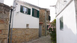 A narrow cobblestone street with stone buildings, a small window, and a flower box with pink flowers. - 9, Cimo da aldeia (Aldeia de João Pires)