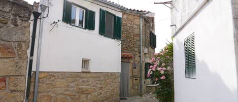 A narrow cobblestone street with stone buildings, a small window, and a flower box with pink flowers.