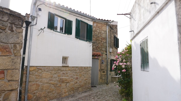 A narrow cobblestone street with stone buildings, a small window, and a flower box with pink flowers.