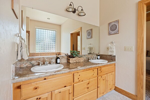 A bathroom with two sinks, wooden cabinets, a large mirror, and a window with a view.