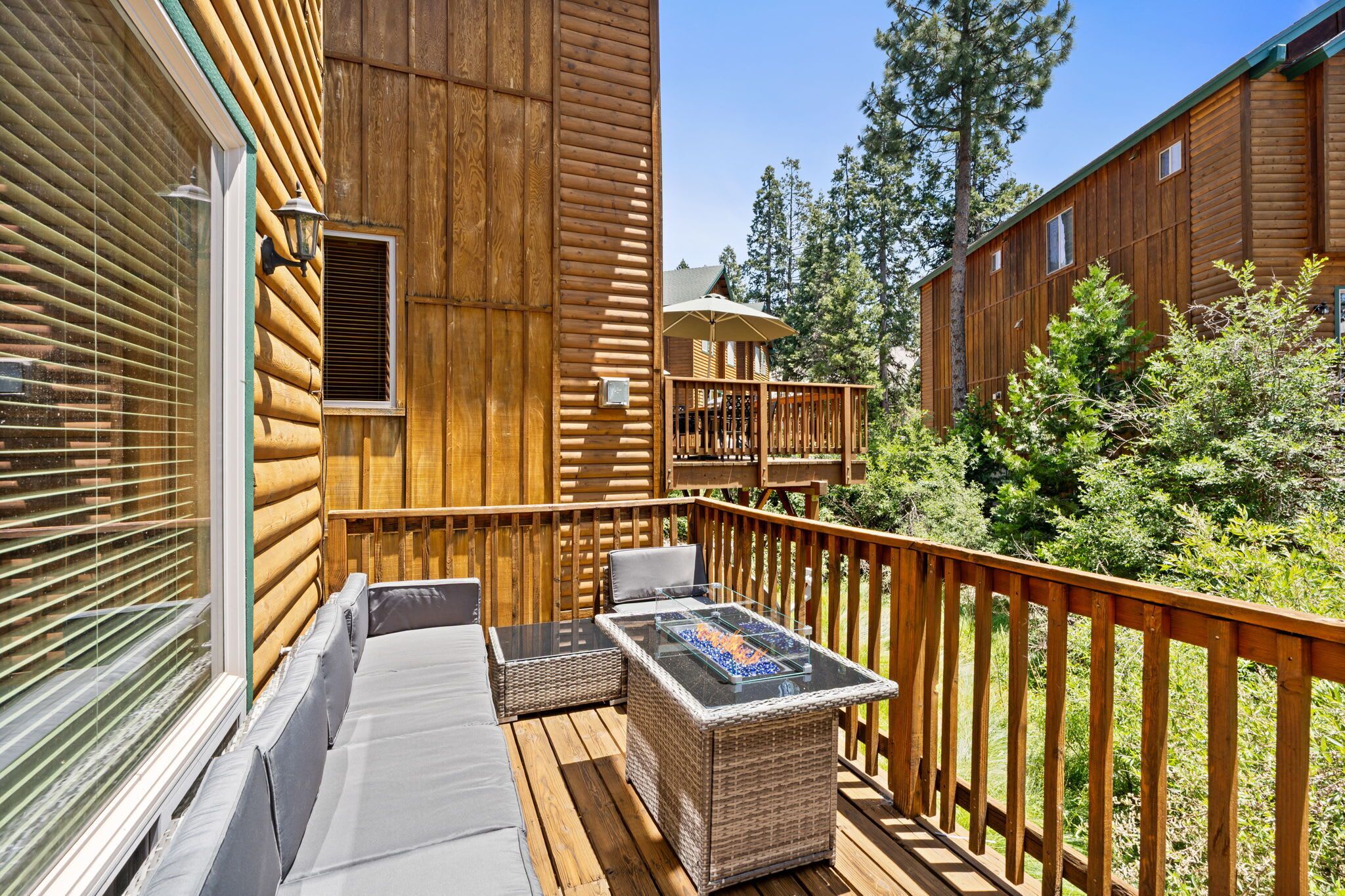 A wooden deck with outdoor furniture, a glass-top table, and a built-in fire feature.