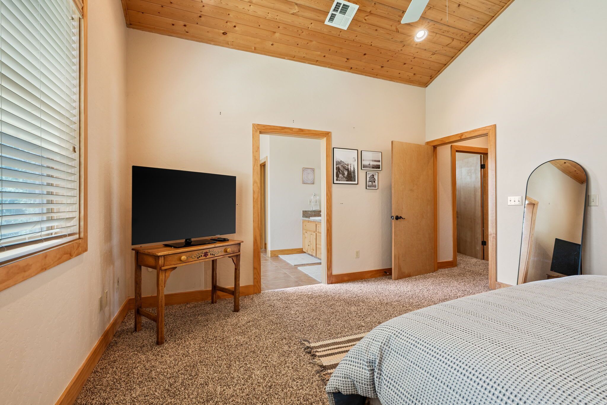 A bedroom with a wooden ceiling, a television on a wooden table, a bed, and a door leading to a bathroom.