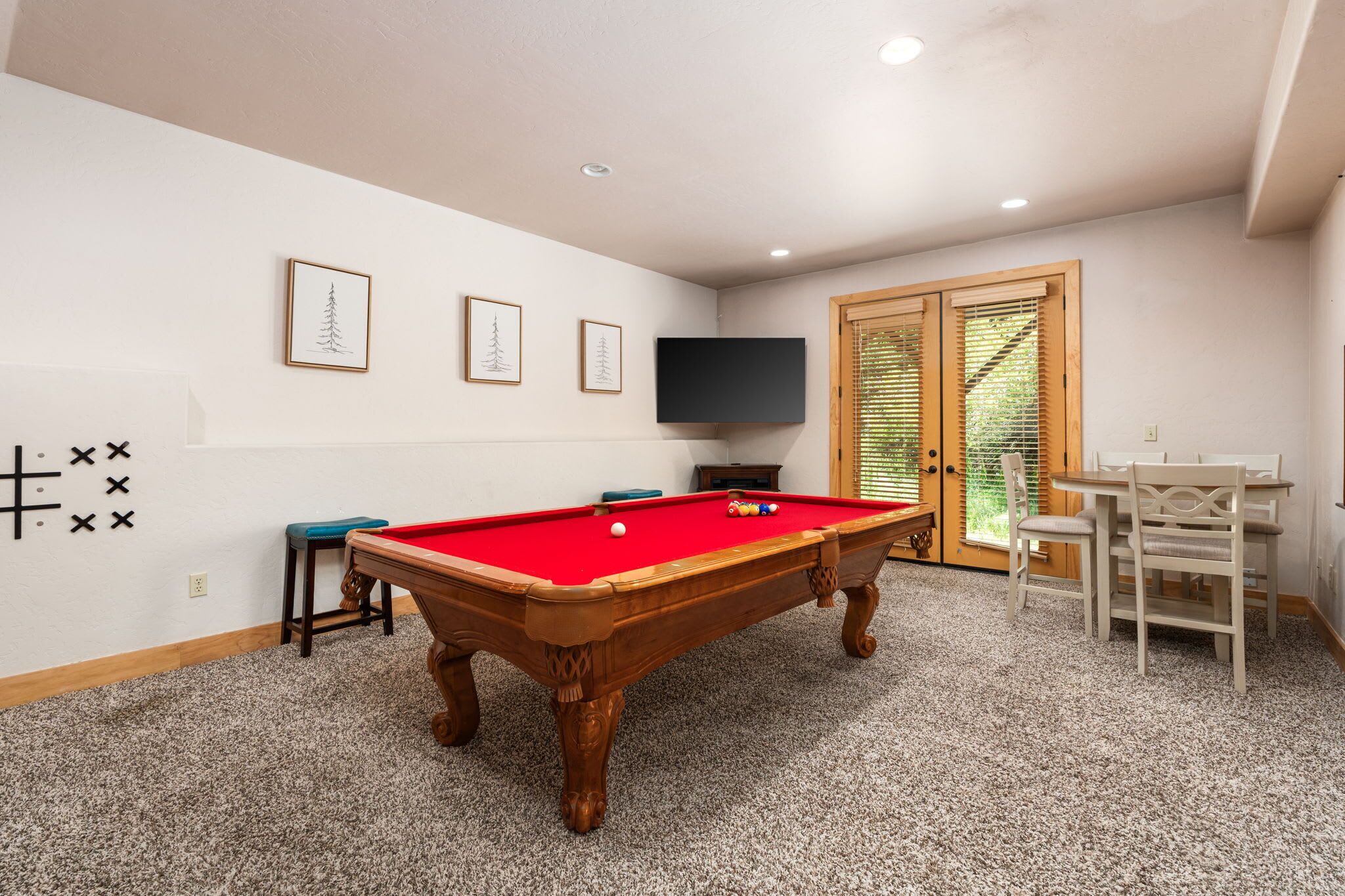 A pool table in a room with a carpeted floor, a television mounted on the wall, and a door with blinds.