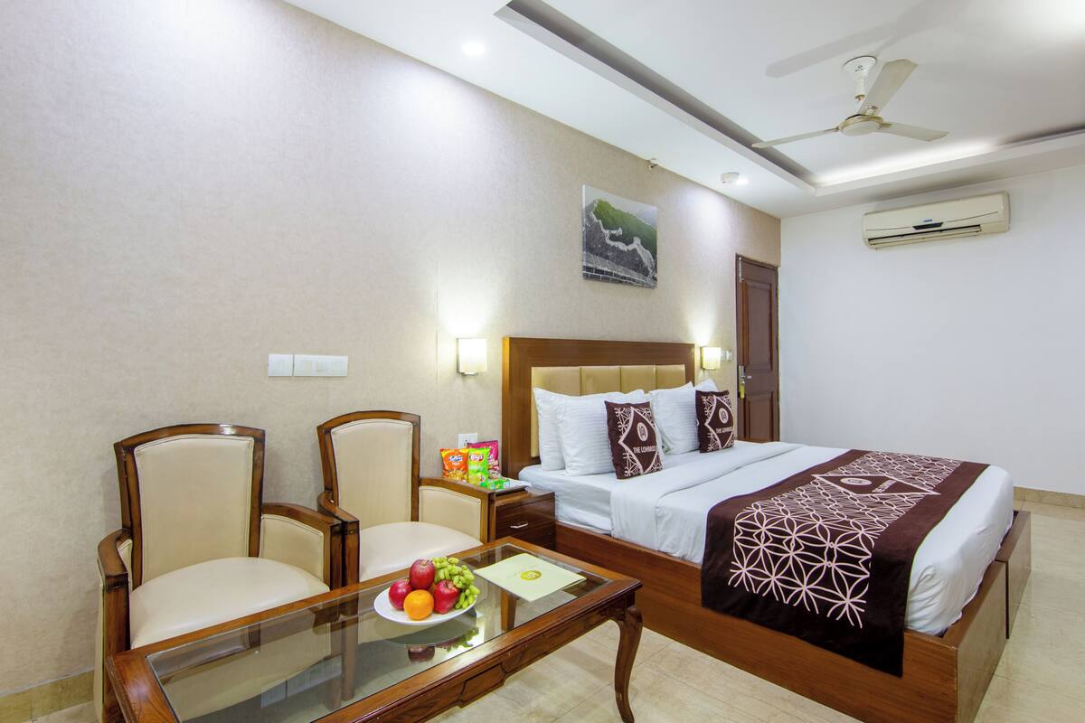 A hotel room with a bed, two chairs, a glass table with fruit, and a ceiling fan.