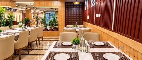 A restaurant with multiple tables set for dining, featuring a modern interior with wooden accents and potted plants.