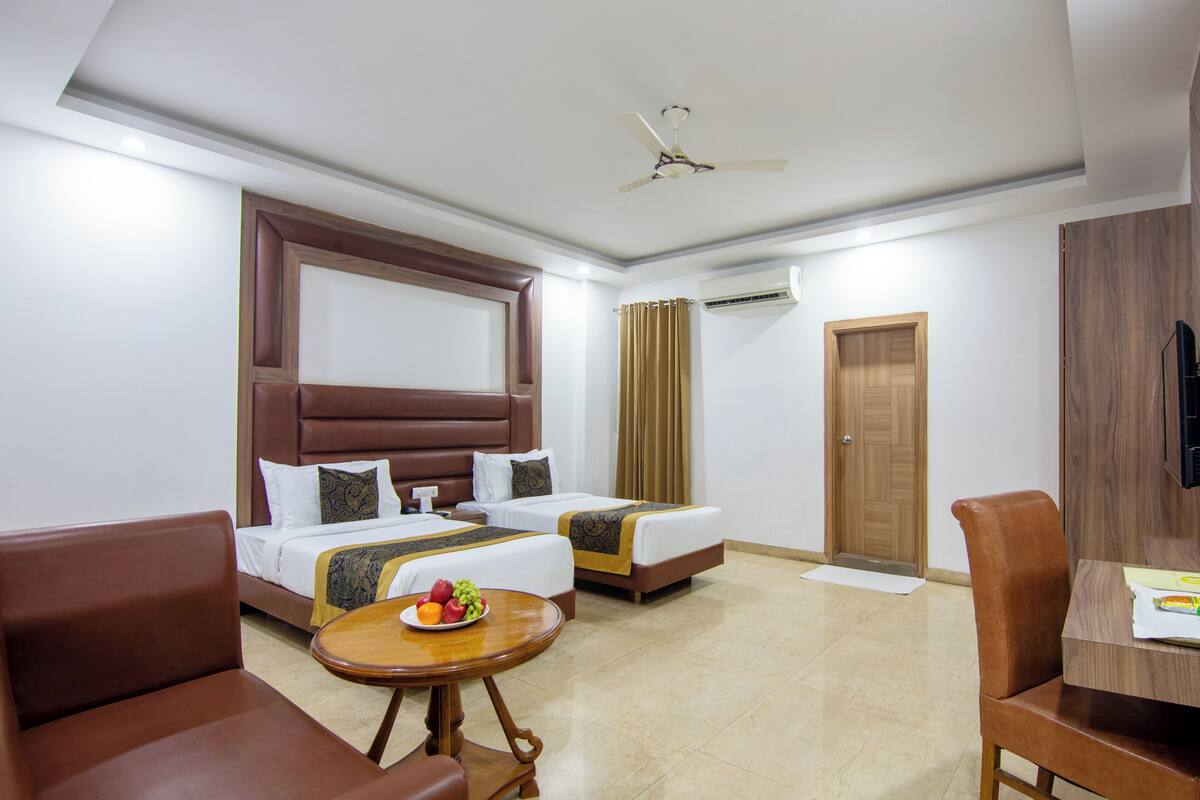 A hotel room with two beds, a dining table, a chair, and a small round table with fruit.