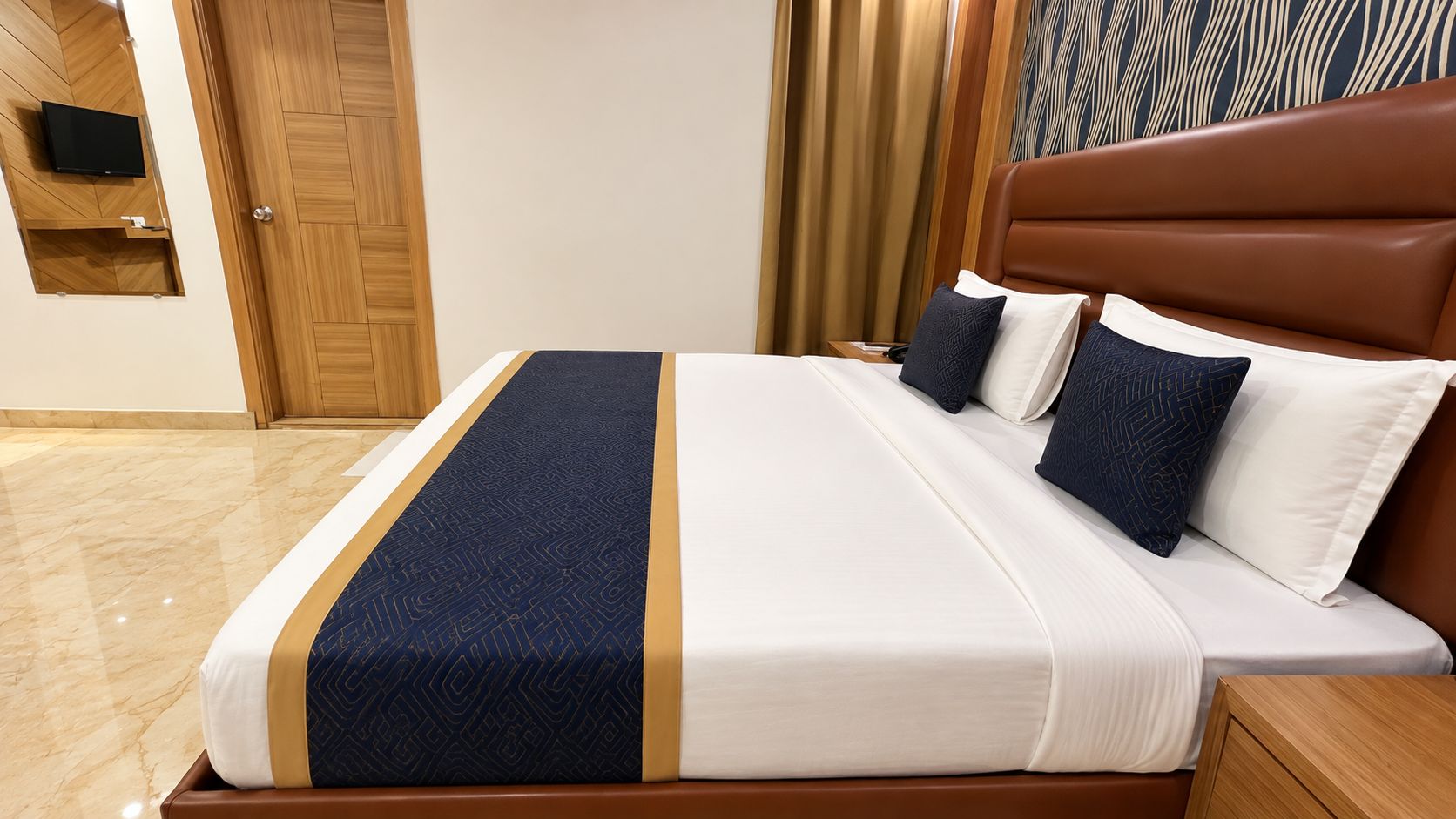 A hotel room with a bed, wooden headboard, and a flat-screen TV mounted on the wall.