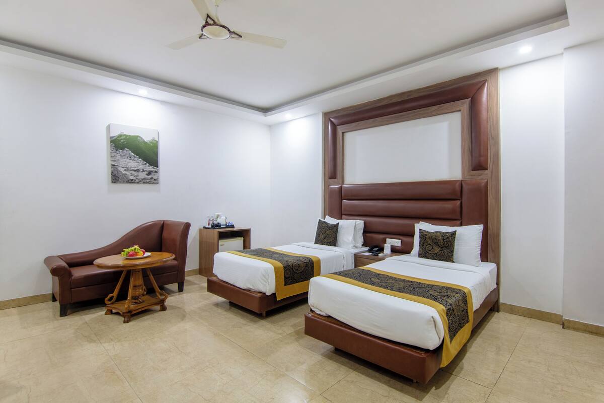 A hotel room with two beds, a sofa, a small round table, and a ceiling fan.