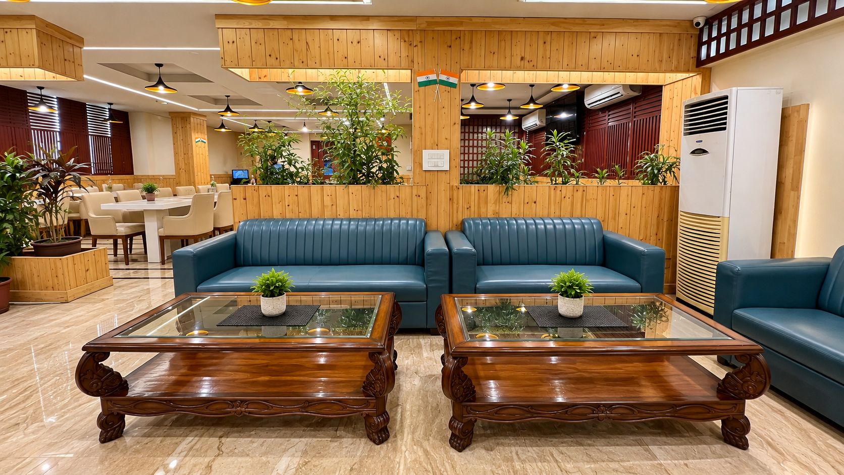 Um hall com painéis de madeira, sofás de couro azul e duas mesas de centro de vidro com plantas em vasos.