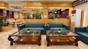 Eine Lobby mit Holzwandverkleidung, blauen Ledersofas und zwei Glastischen mit Blumentöpfen.