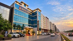 A modern hotel building with a glass facade, a red carpet entrance, and multiple parked cars. - Hotel Lohmod (New Delhi)