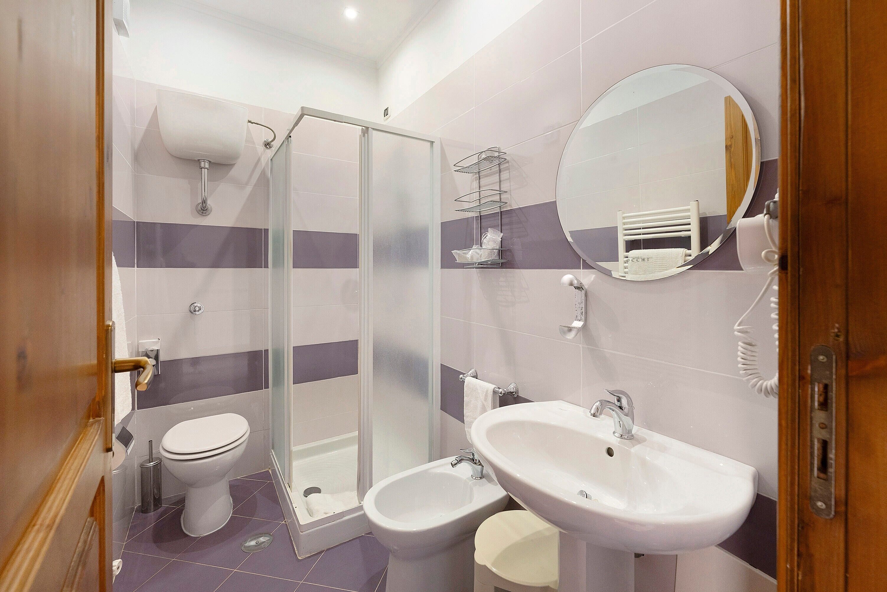 Baño con inodoro, bidé, lavabo, espejo y cabina de ducha.