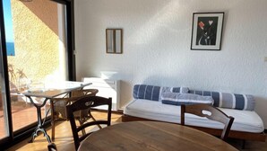 A room with a wooden table and chairs, a sofa with striped cushions, a framed picture on the wall, and a sliding glass door leading to an outdoor area. - Collioure large apartment terrace swimming pool garage air-conditioning exceptional view. (Collioure)