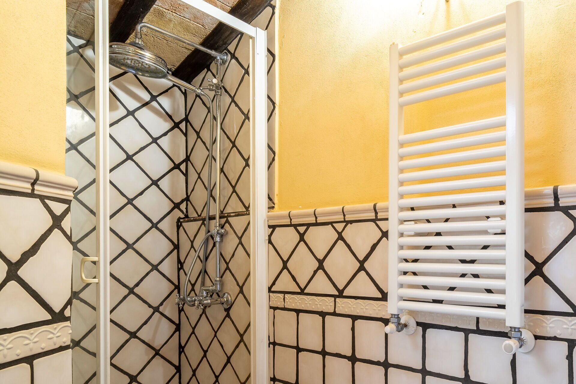 A bathroom with a shower, a white towel rack, and a tiled wall with a geometric pattern.