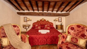 Un dormitori amb un llit gran, dues cadires ornamentades, una taula petita i un sostre de fusta.