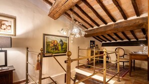 Habitació rústica amb bigues de fusta a la vista, un candelabro i un quadre de cavalls.