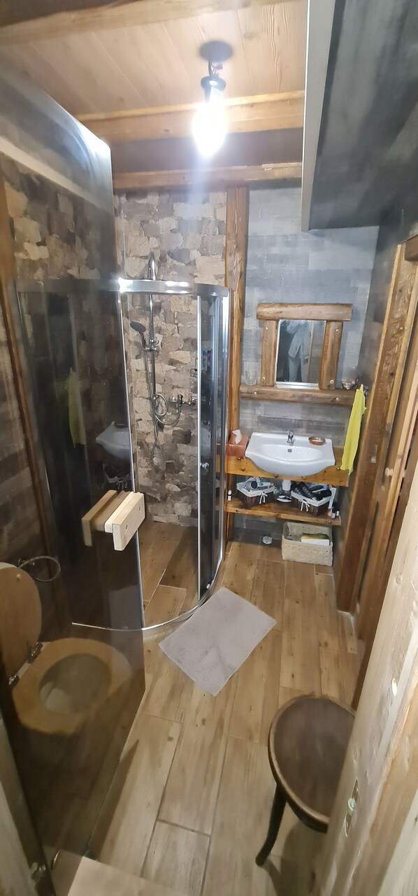 Un baño con ducha envuelta en vidrio, suelo de madera, lavamanos y espejo.