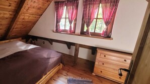 A bedroom with a sloped ceiling, a bed, a wooden dresser, and a window with curtains.