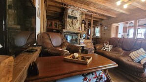 A cozy cabin interior with a leather sofa, a wooden coffee table with snacks, and a stone fireplace.