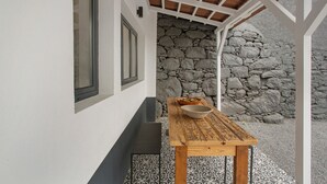 A covered outdoor seating area with a stone wall, a wooden table, and a bowl.