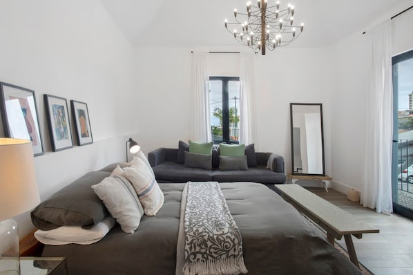 Un dormitorio moderno con cama, sofá, banqueta, candelabro y un ventanal grande.