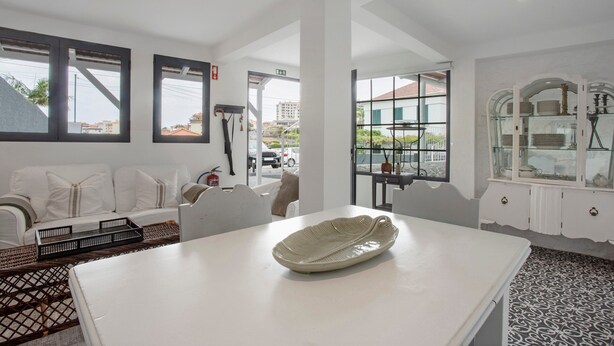 A hotel room with a white sofa, a dining table with a decorative bowl, a patterned floor, and a view of the outside.