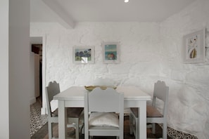 Un comedor con una mesa y sillas blancas, pared blanca con textura y obras de arte enmarcadas.