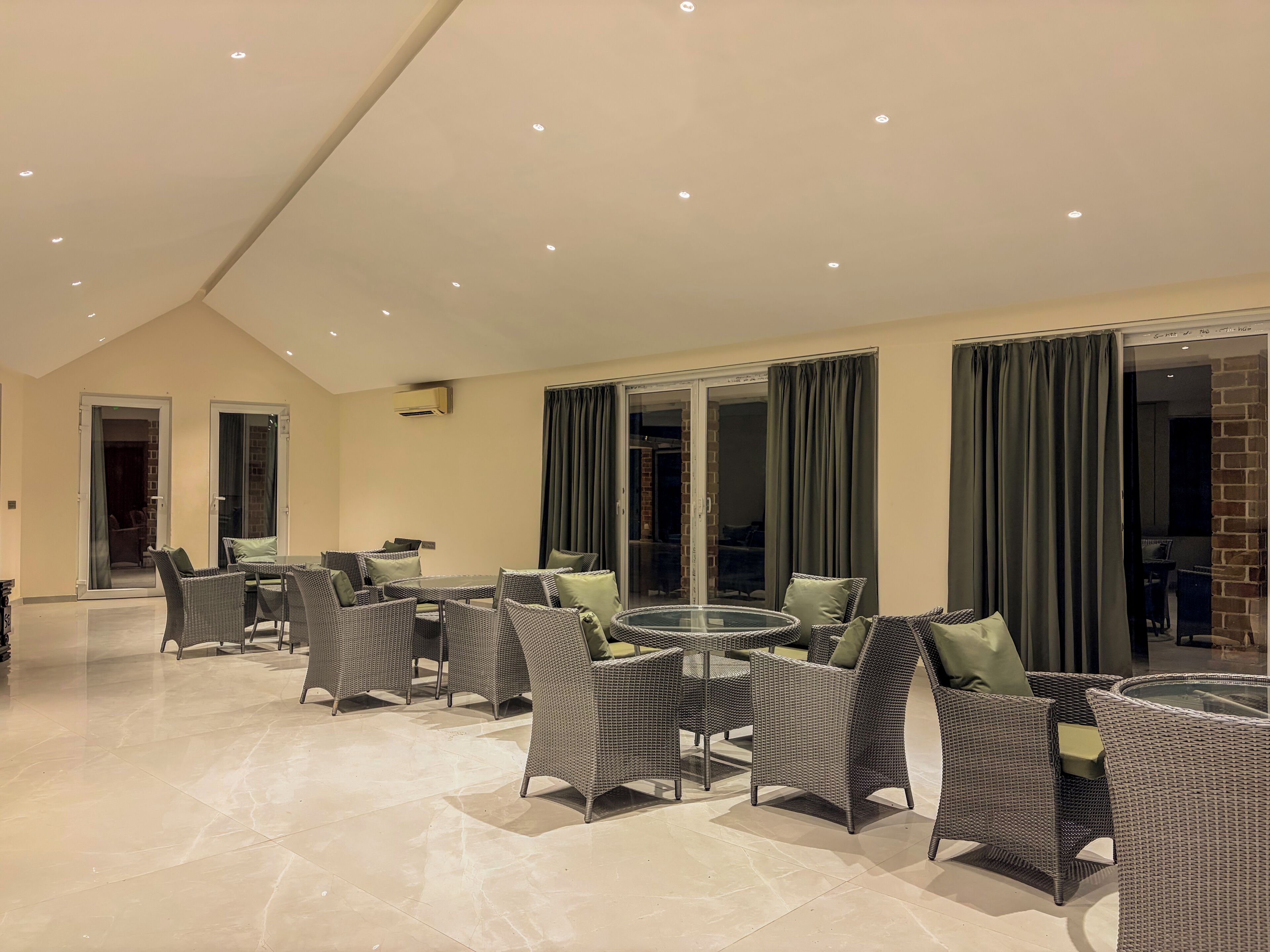 A spacious indoor area with wicker furniture, a glass table, and a ceiling with recessed lighting.
