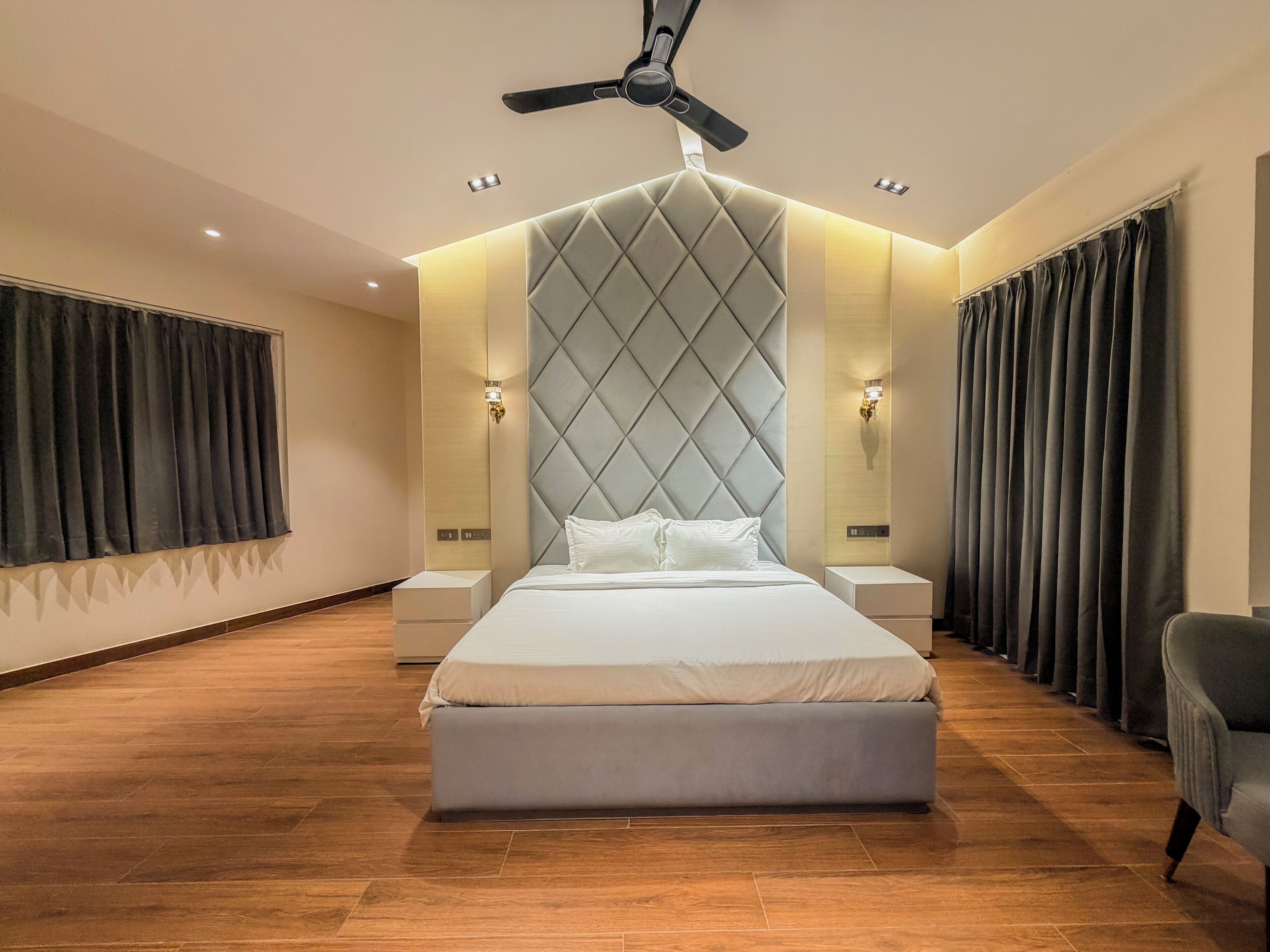 A modern hotel room with a large bed, a ceiling fan, and a view of the city.