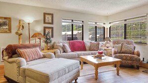 A cozy living room with a sofa, armchair, and ottoman, a wooden coffee table, and a fireplace.